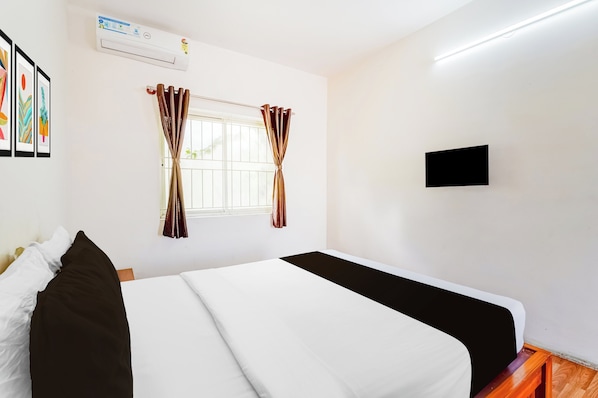 A hotel room with a bed, a window with curtains, a wall-mounted TV, and a ceiling fan.