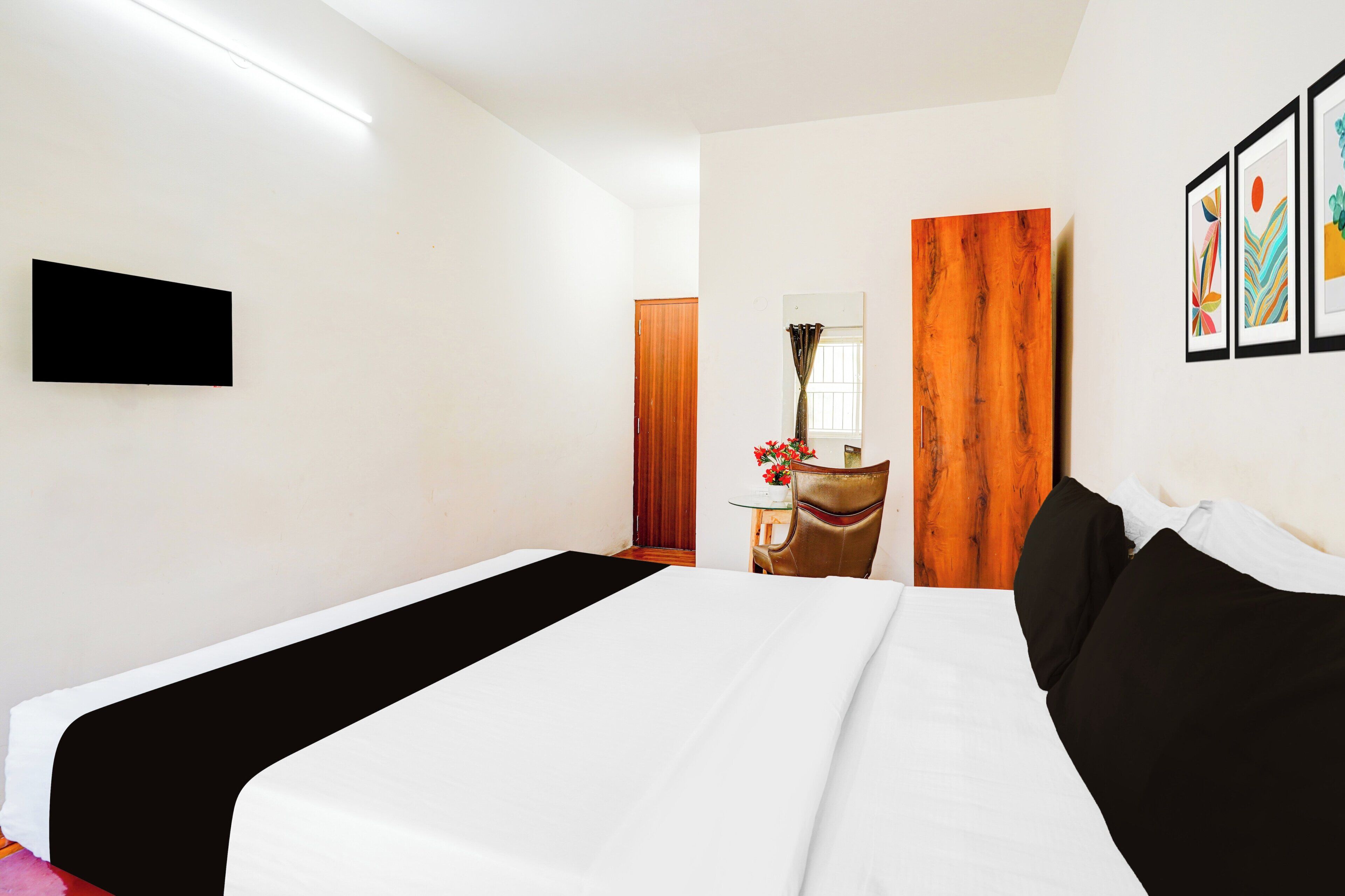 Habitación de hotel con cama, televisor de pantalla plana montado en la pared, puerta de madera y una pequeña mesa con un florero.