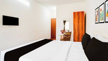 Habitación de hotel con cama, televisor de pantalla plana montado en la pared, puerta de madera y una pequeña mesa con un florero.