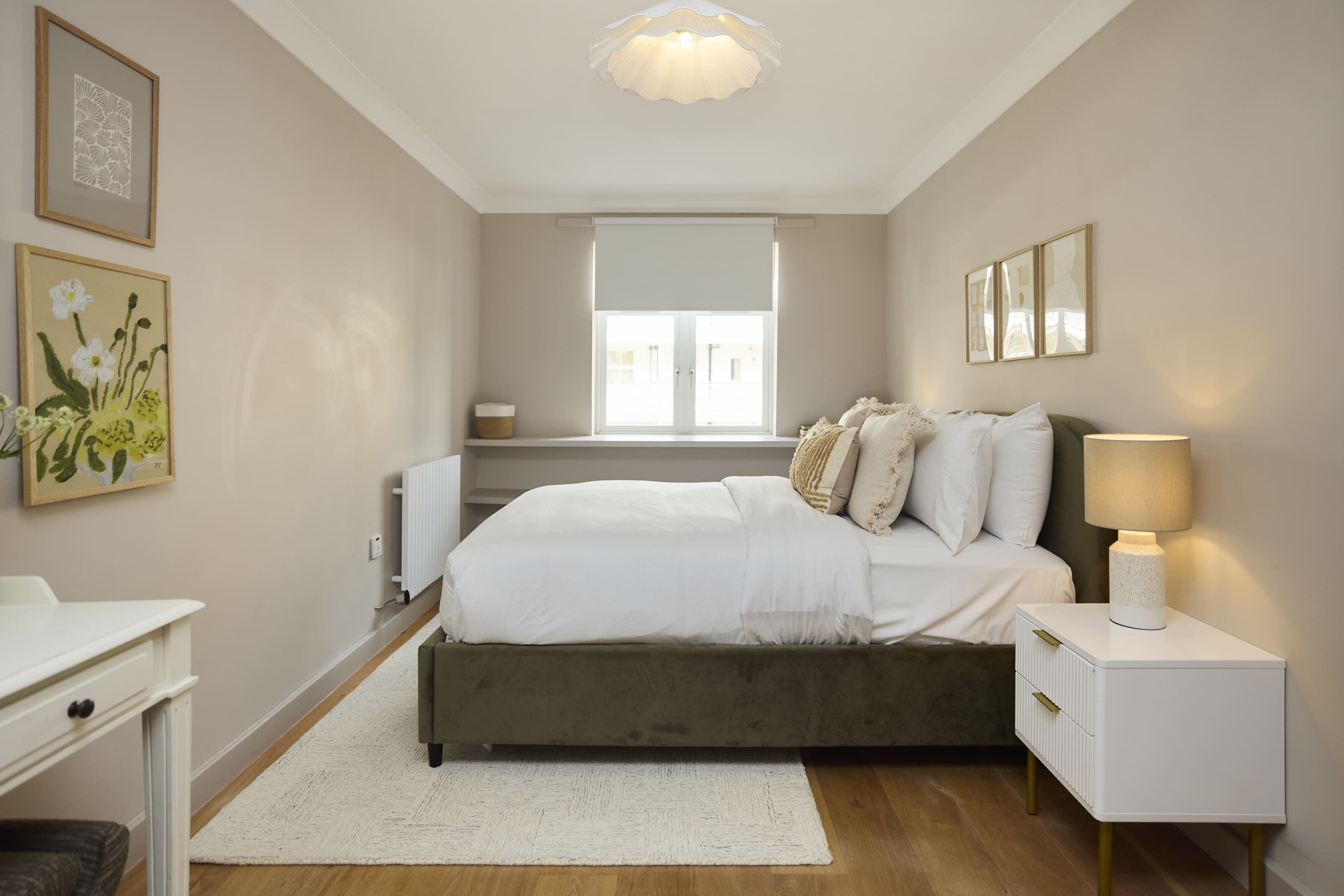A bedroom with a bed, bedside tables, a radiator, a window, and artwork on the walls.