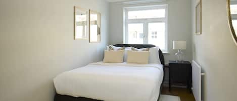 A bedroom with a bed, bedside tables, a window, and a radiator.