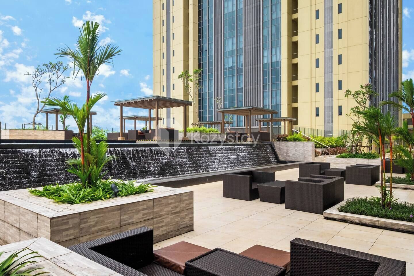 A rooftop patio with outdoor seating, a waterfall feature, and a modern building in the background.
