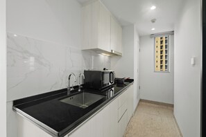 A modern kitchen with a black countertop, stainless steel sink, white cabinets, and a microwave. - Korava by Kozystay - BSD (Tangerang)