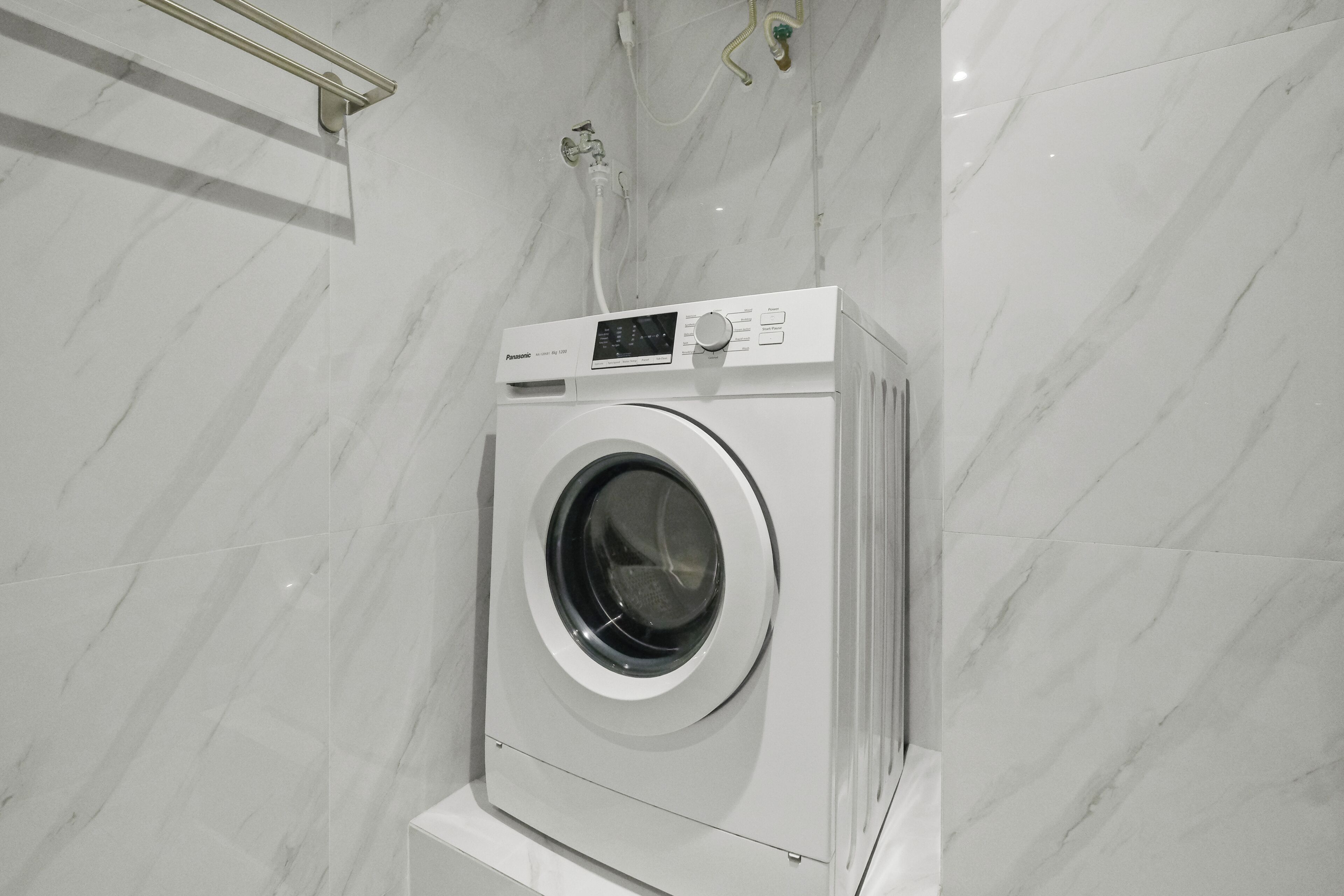A front-loading washing machine in a bathroom with a marble wall.