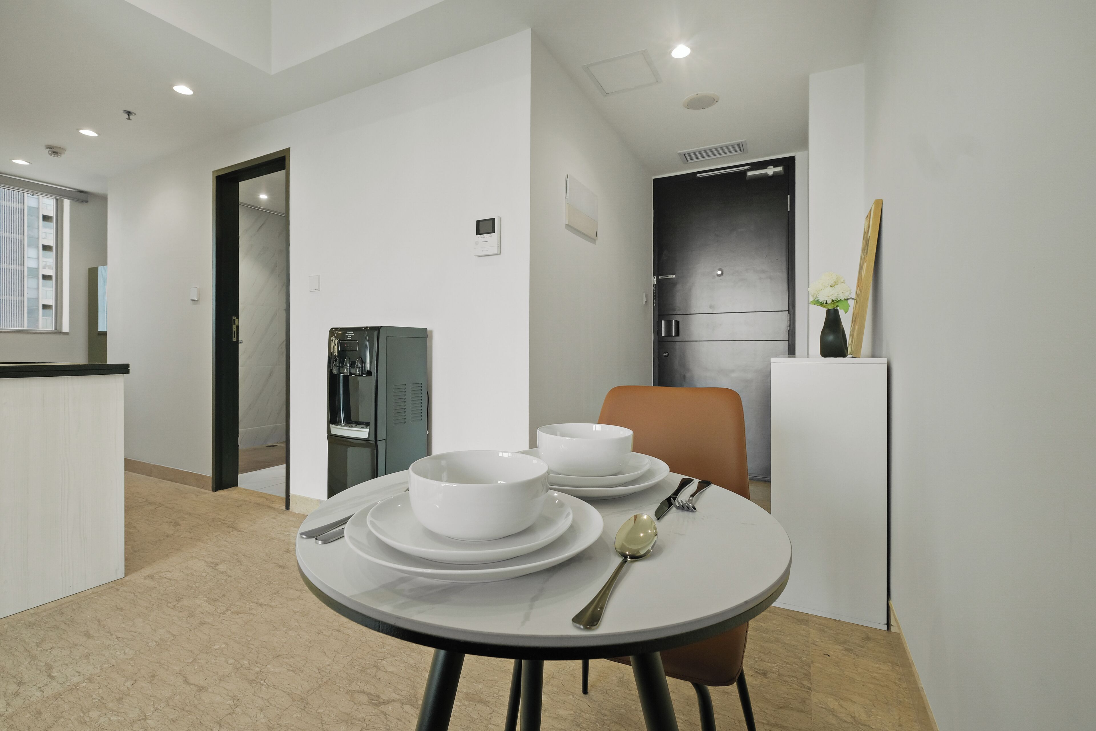 A modern kitchen with white cabinetry, a built-in refrigerator, and a dining area with a round table set for two.