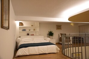 A bedroom with a bed, bedside tables, a crib, a shelf with decorative items, and a wall-mounted light fixture. - House Domusella Apartment, in the heart of Rome—quiet and comfortable (Roma)