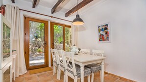 A dining area with a white table and chairs, a hanging pendant light, and a stone wall with a painting. - Villa Near Pollensa Old Town (Pollença)