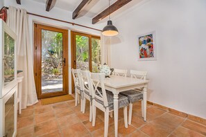 A dining area with a white table and chairs, a hanging pendant light, and a stone wall with a painting. - Villa Near Pollensa Old Town (Pollença)
