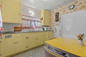A kitchen with yellow cabinets, a microwave, a sink, and a clock on the wall. - Sierra Retreat Motel (Coleville)