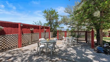 A patio with tables and chairs, a wooden fence, and trees.