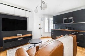 A modern kitchen with dark cabinetry, a built-in oven, and a coffee maker. - Cozy Apartment 1br/4p - La Villette (Paris)