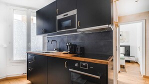 A modern kitchen with black cabinets, a wooden countertop, a microwave, a coffee maker, and an oven. - Cozy Apartment 1br/4p - La Villette (Paris)