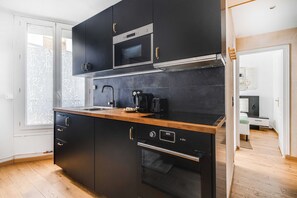 A modern kitchen with black cabinets, a wooden countertop, a microwave, a coffee maker, and an oven. - Cozy Apartment 1br/4p - La Villette (Paris)