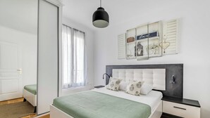 A bedroom with a bed, bedside tables, a nightstand, a window with curtains, a wall-mounted light, and a decorative piece above the bed. - Cozy Apartment 1br/4p - La Villette (Paris)