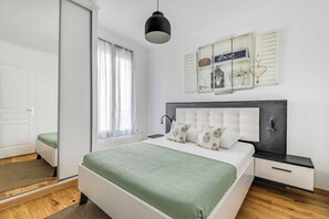 A bedroom with a bed, bedside tables, a nightstand, a window with curtains, a wall-mounted light, and a decorative piece above the bed. - Cozy Apartment 1br/4p - La Villette (Paris)