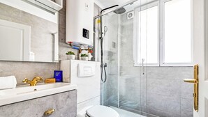 A modern bathroom with a glass shower enclosure, a white toilet, and a vanity with a gold faucet. - Cozy Apartment 1br/4p - La Villette (Paris)