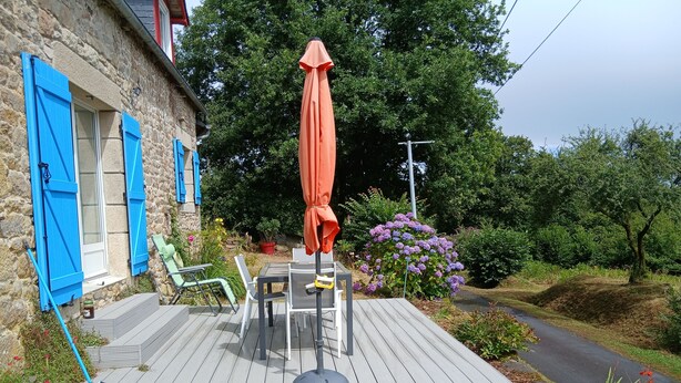 Una terraza de madera con mobiliario exterior y una mesa, rodeada por un jardín con diversas plantas y flores.
