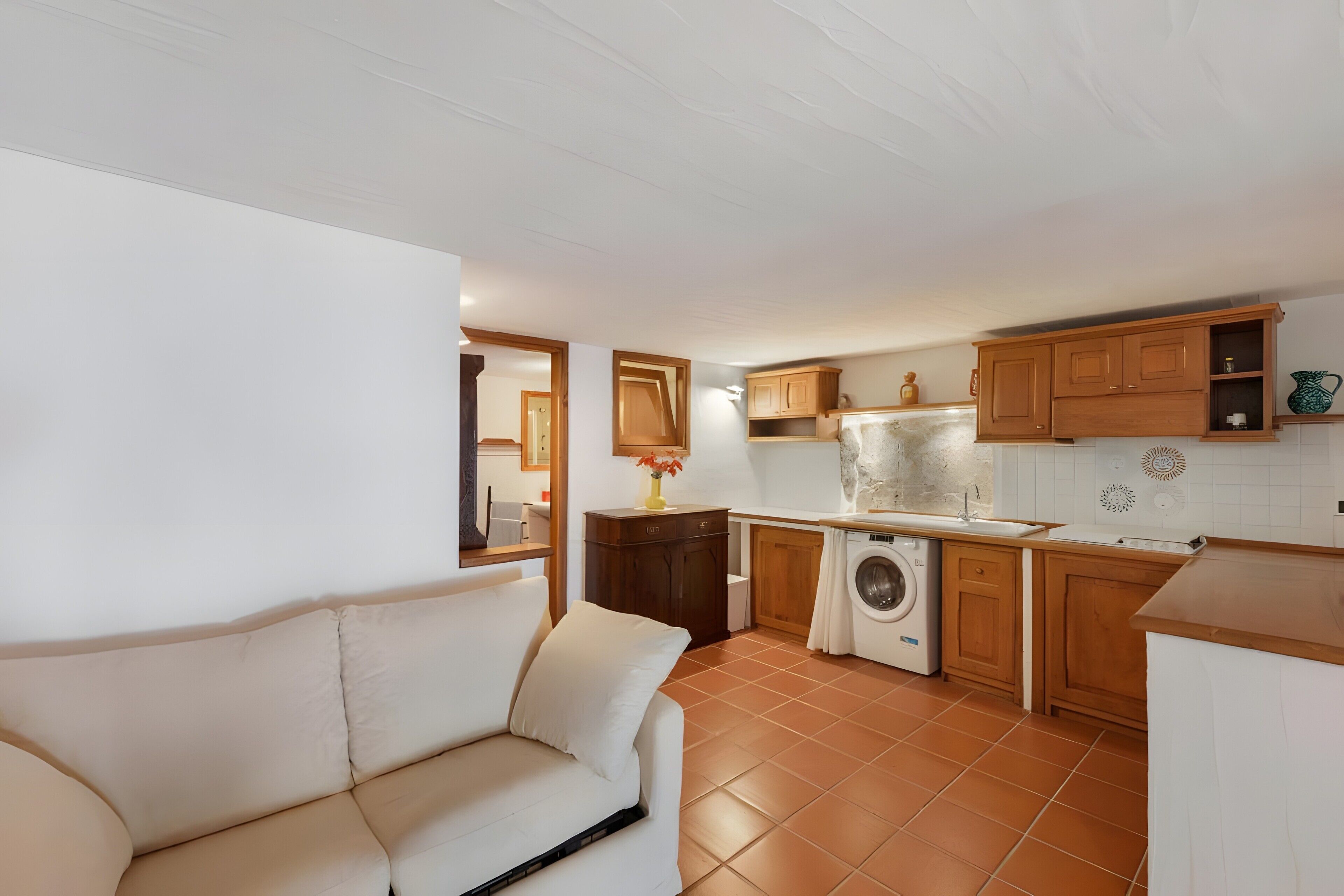 Una cucina compatta con lavatrice, mobili in legno e schienale rivestito di piastrelle bianche.