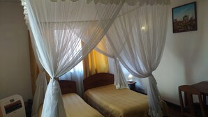 A room with a bed under a canopy, a bedside table with a lamp, and a chair. - ivotel  (Antananarivo)