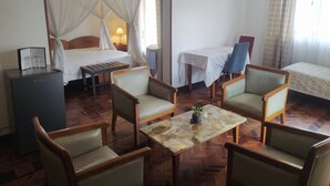 A hotel room with a bed, a desk, a chair, a small table, and a nightstand. - ivotel  (Antananarivo)