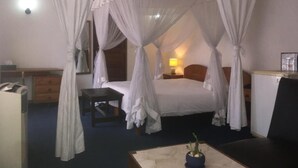 A hotel room with a four-poster bed, bedside tables, a desk, and a chair. - ivotel  (Antananarivo)