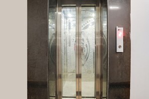An elevator with a marble wall and a control panel with a red light. - Collection O Gol Park Atala (Prayagraj)
