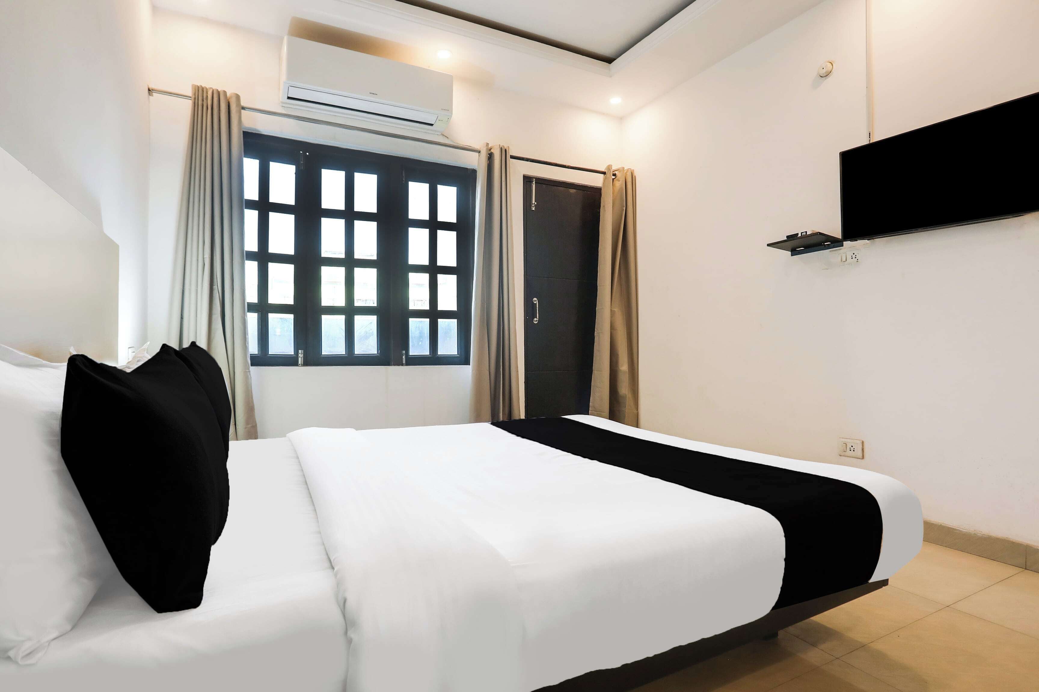 A hotel room with a bed, curtains, an air conditioning unit, a window with a view, and a mounted television.