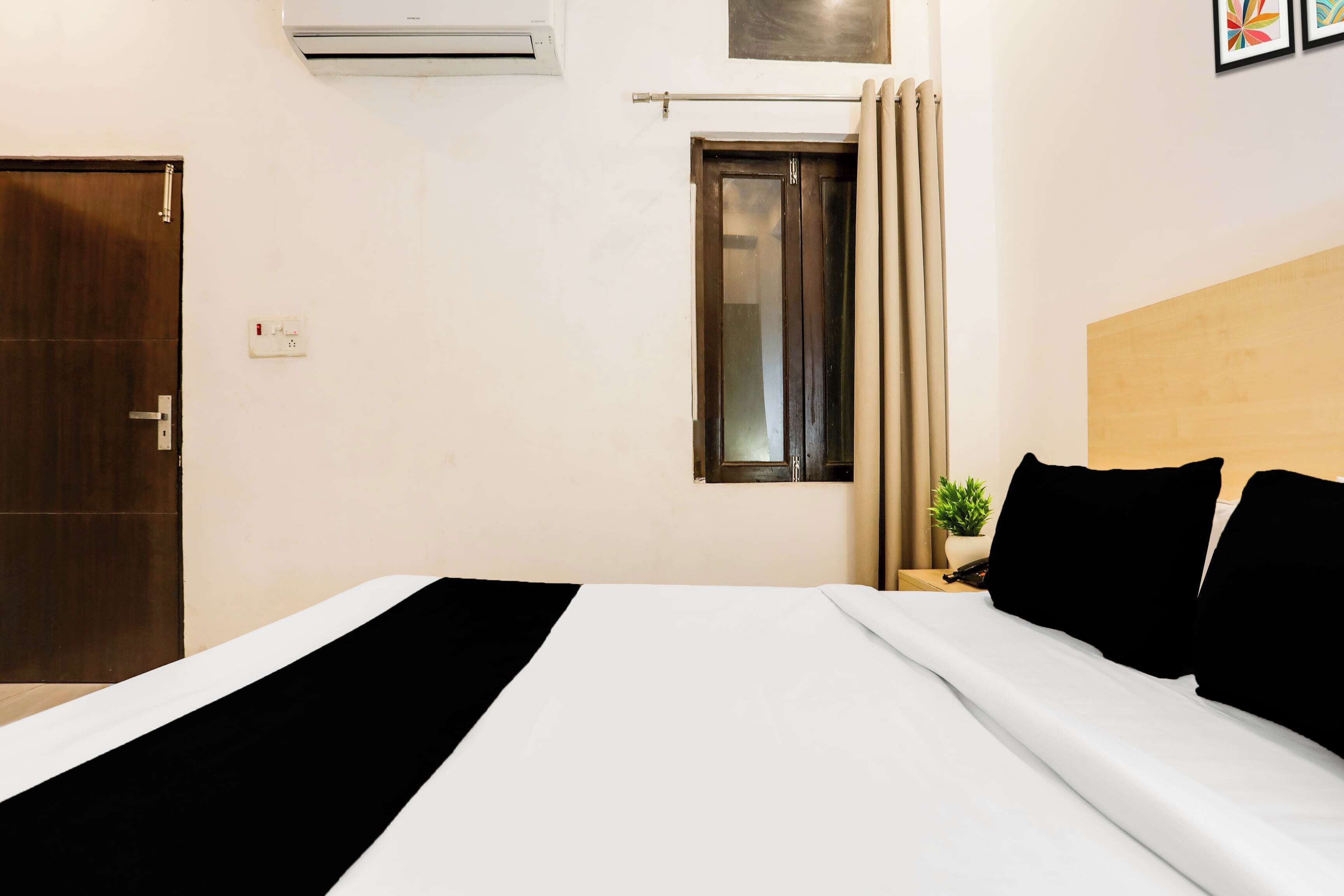 Habitación de hotel con cama, ventana con cortinas, puerta y equipo de aire acondicionado en la pared.
