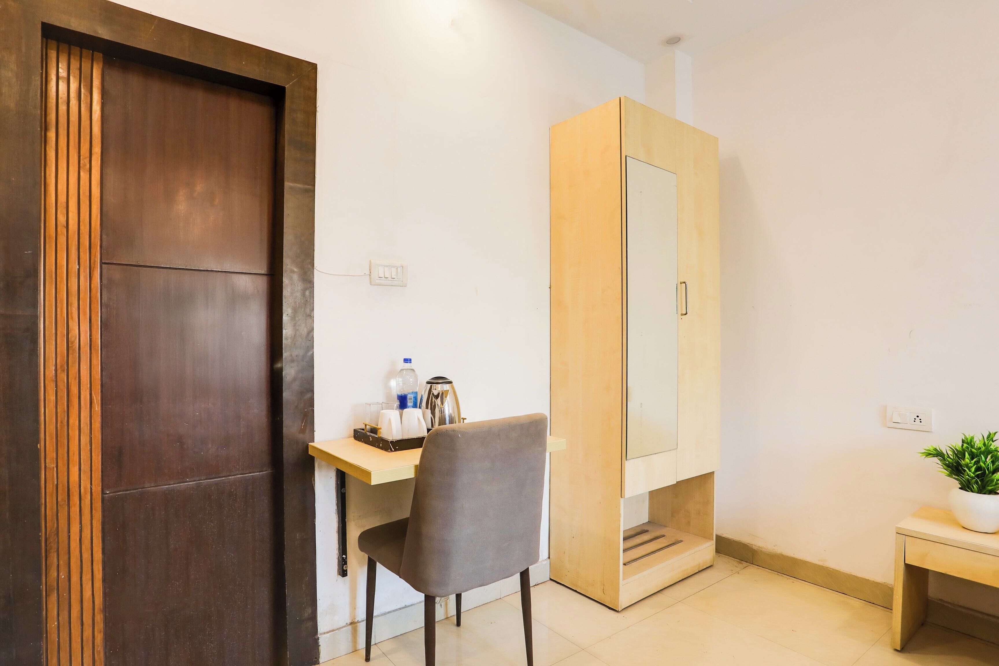 Una habitación con puerta de madera, un escritorio con silla, una mesita con planta y un armario con espejo.