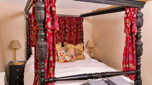 A four-poster bed with red curtains, a wooden headboard, and floral bedding. - Finest Retreats | Lavender Cottage (Methwold)