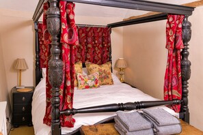 Ein Bett mit Baldachin, ausgestattet mit roten Vorhängen, einem Holz-Kopfteil und floralem Bettbezug.