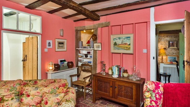 A cozy room with a wooden ceiling, a floral sofa, a wooden cabinet, and a bookshelf. - Finest Retreats | Lavender Cottage (Methwold)