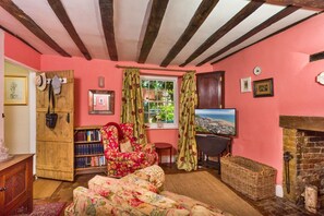 Ein gemütliches Wohnzimmer mit Kamin, Fernseher, Bücherregal und einem blumigen Sessel.