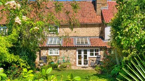 A stone house with a tiled roof, a garden with various plants, and a patio with outdoor furniture. - Finest Retreats | Lavender Cottage (Methwold)