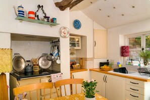 A kitchen with a dining table, chairs, a stove, and various kitchen utensils. - Lavender Cottage (Methwold)