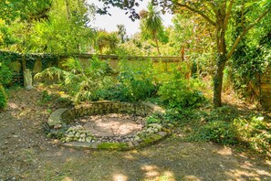 Ein Garten mit einem kreisförmigen Steinelement, umgeben von verschiedenen Pflanzen und Bäumen.