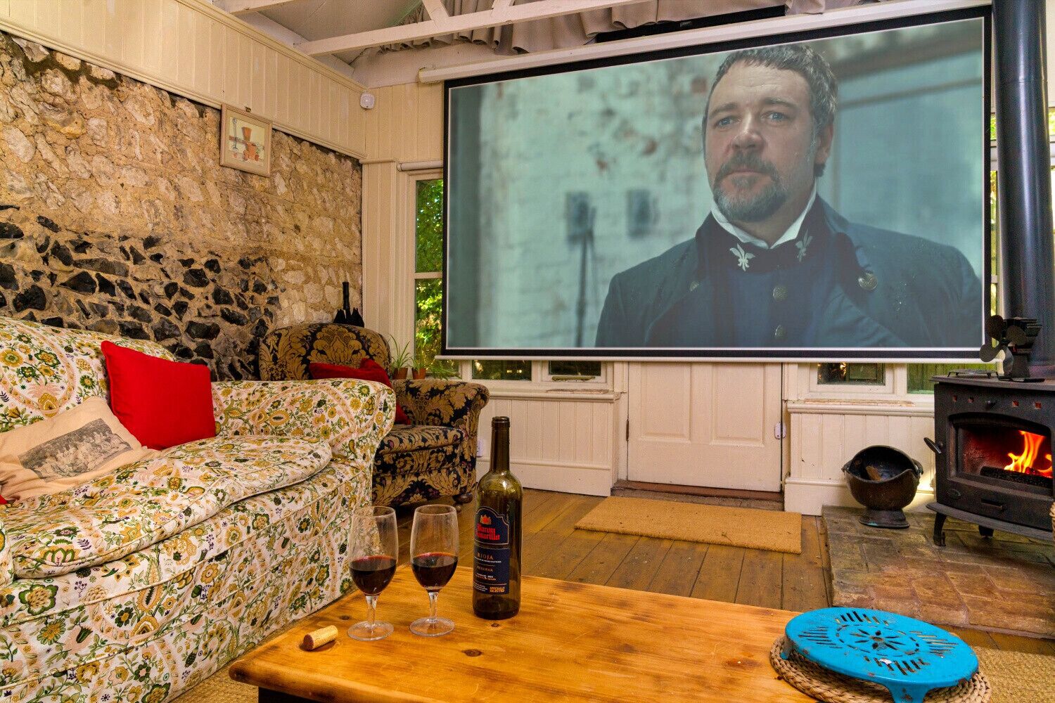 Una sala de estar acogedora con una pared de piedra, un sofá con tapicería floral, una mesa de centro de madera con copas de vino y una chimenea.