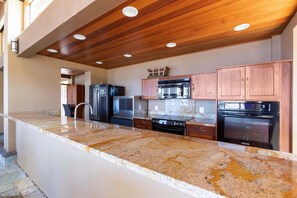 A modern kitchen with granite countertops, stainless steel appliances, and wooden cabinetry. - Wailea Elua 1104 - Ocean Views, Central A/C, Walk to Ulua Beach, Shops & Dining! (Kihei)