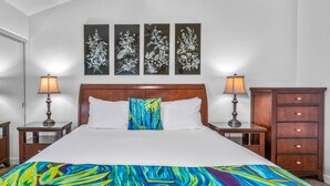 A hotel room with a large bed, two bedside tables, a nightstand, a dresser, and three wall-mounted artworks. - Wailea Elua 1104 - Ocean Views, Central A/C, Walk to Ulua Beach, Shops & Dining! (Kihei)