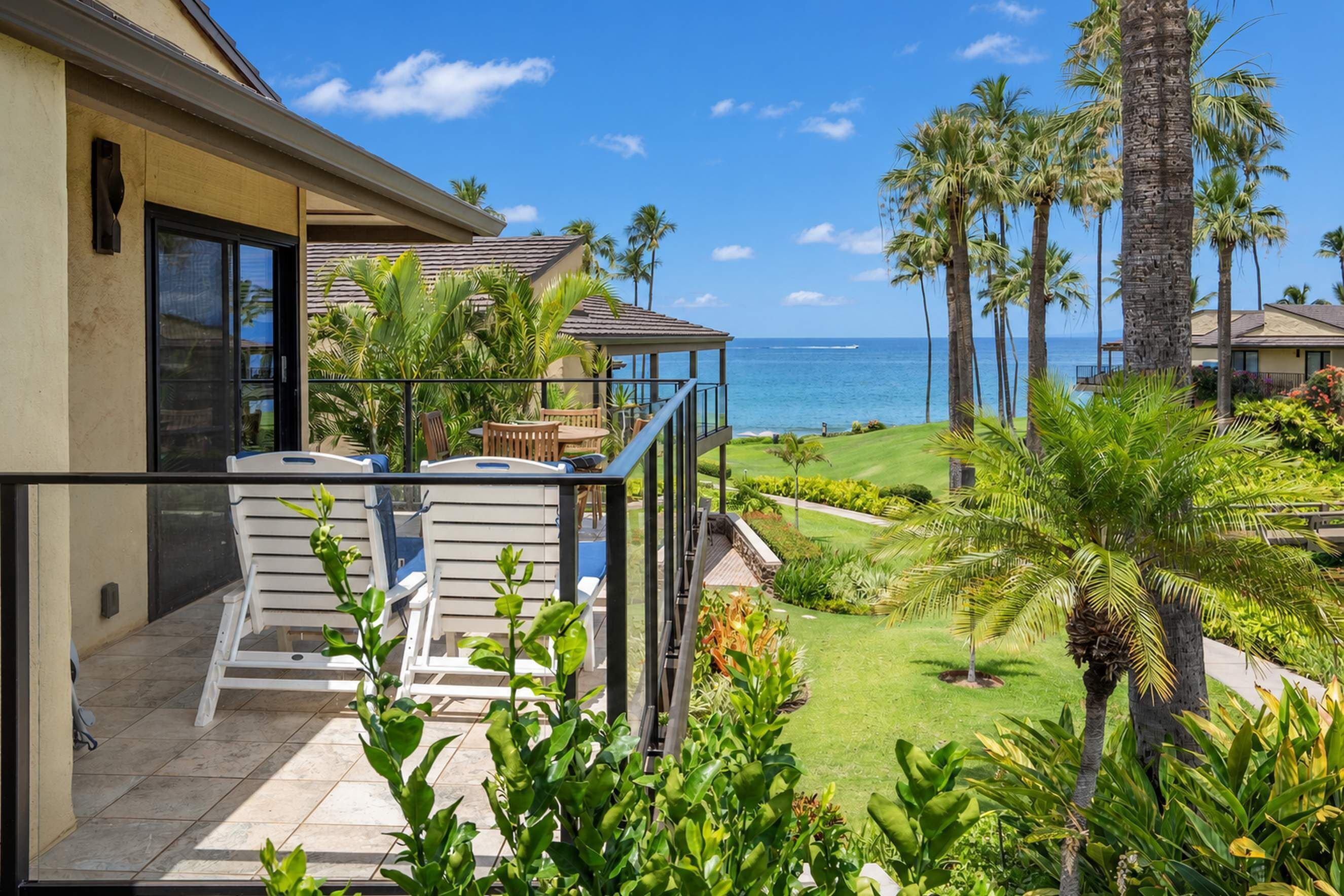 A balcony with outdoor furniture overlooking a well-maintained lawn and a view of the ocean.