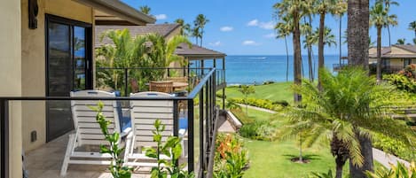A balcony with outdoor furniture overlooking a well-maintained lawn and a view of the ocean.