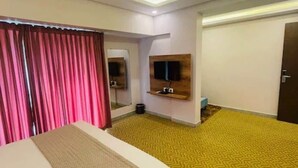 A hotel room with a bed, a television mounted on the wall, a mirror, and a yellow patterned carpet. - Collection O Kengeri Bus Terminal (Bangalore)
