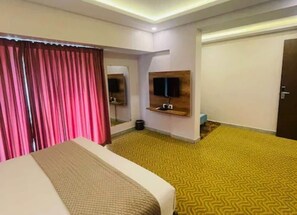 Une chambre d’hôtel avec un lit, un téléviseur fixé au mur, un miroir et une moquette  à motifs jaunes.
