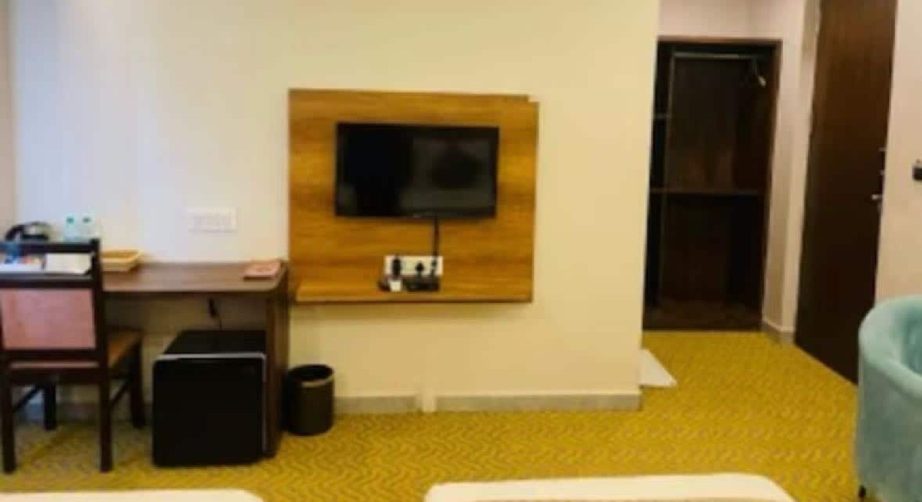 A hotel room with a bed, a desk, a chair, a television mounted on the wall, and a door.