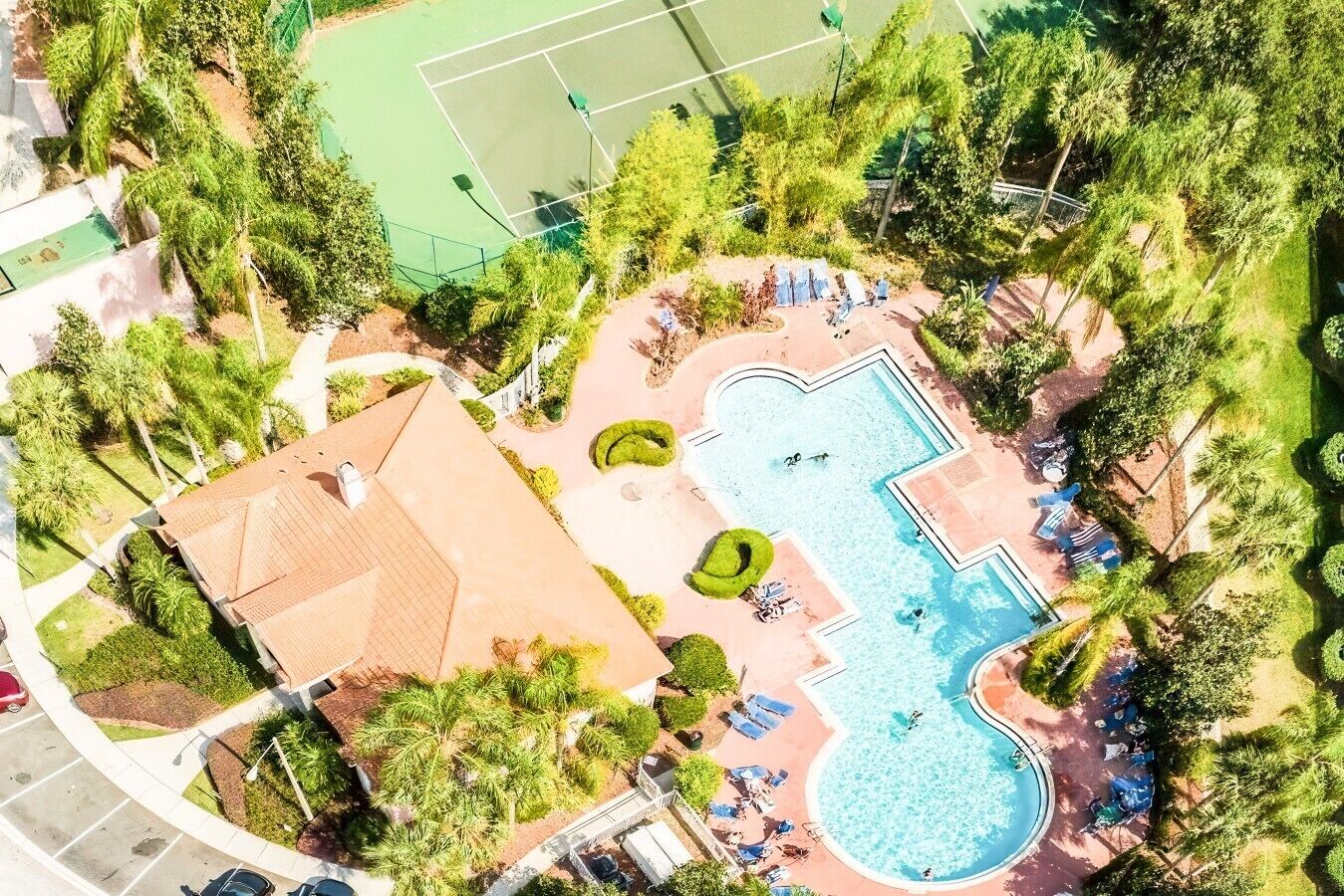 An aerial view of a resort with a swimming pool, tennis courts, and landscaped areas.