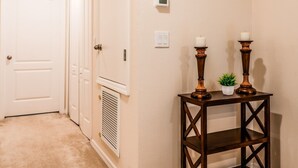 A hallway with beige walls, a white door, a thermostat, and a small table with candles. - Tranquil Vacations - Kissimmee (Kissimmee)