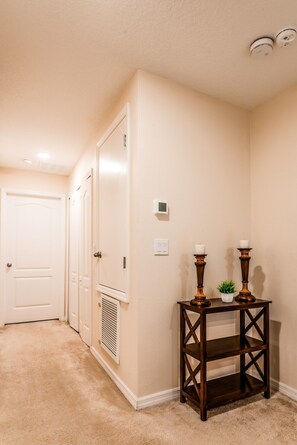 A hallway with beige walls, a white door, a thermostat, and a small table with candles. - Tranquil Vacations - Kissimmee (Kissimmee)