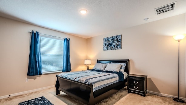 A bedroom with a bed, bedside table, lamp, and artwork on the wall. - Tranquil Vacations - Kissimmee (Kissimmee)
