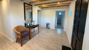 A room with a wooden floor, a black door, a mirror, a wicker chair, and a table with decorative items. - Panoramic ocean view, direct access to a private sandy beach in Skagen South—family-friendly (Ålbæk)