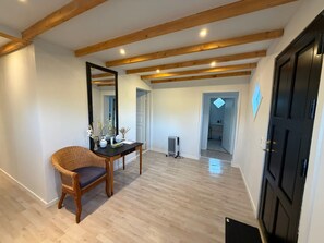 A room with a wooden floor, a black door, a mirror, a wicker chair, and a table with decorative items. - Panoramic ocean view, direct access to a private sandy beach in Skagen South—family-friendly (Ålbæk)